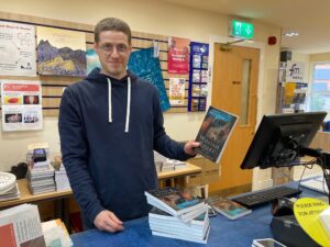 John Townend, general manager of Faith Mission Book Shop, Edinburgh stands at till holding a copy of William Ridley and the Celtic Cross.