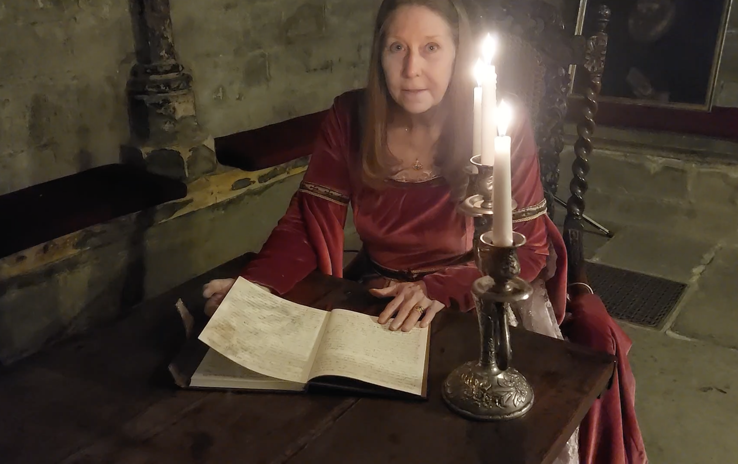 Connie MacLeod - Author Songwriter sits by candlelight reading the Gospel of John at Glasgow Cathedral. She is wearing a handmade cerise medieval gown.